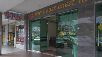 The entrance of Hotel Rose Crest Hill with a visible sign for Num Song Apartment and a glass door reflecting a car and a building.