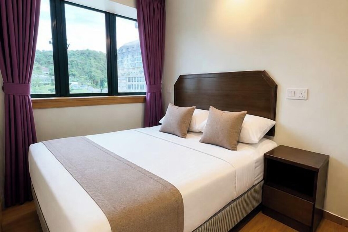 A hotel room with a bed, a nightstand, and a window with curtains.