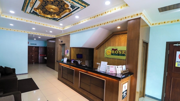 Een hotel receptie met een houten balie, een bord met Hotel Rose Crest Hill en een receptiecounter.
