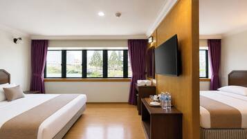 Quarto de hotel com duas camas, televisão de tela plana, uma mesinha com produtos de higiene e uma janela com cortinas.