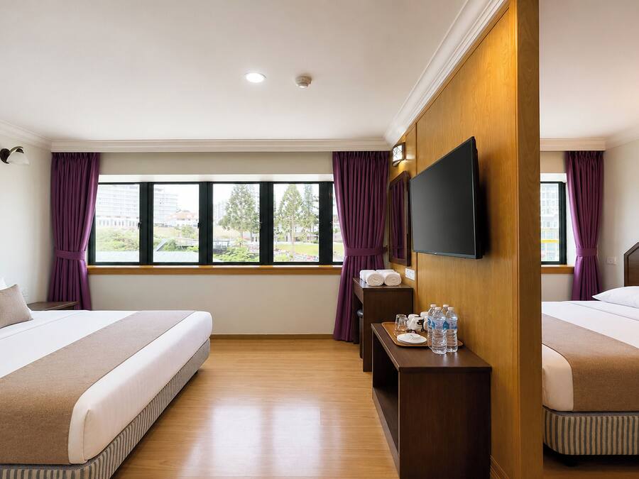 Ein Hotelzimmer mit zwei Betten, einem Flachbildfernseher, einem kleinen Tisch mit Pflegeartikeln und einem Fenster mit Vorhängen.