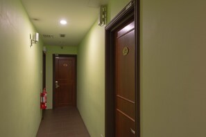A hallway with green walls, a wooden door with a number plate, and a fire extinguisher on the left.