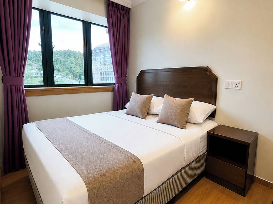 A hotel room with a large bed, a nightstand, a window with curtains, and a wall-mounted light.