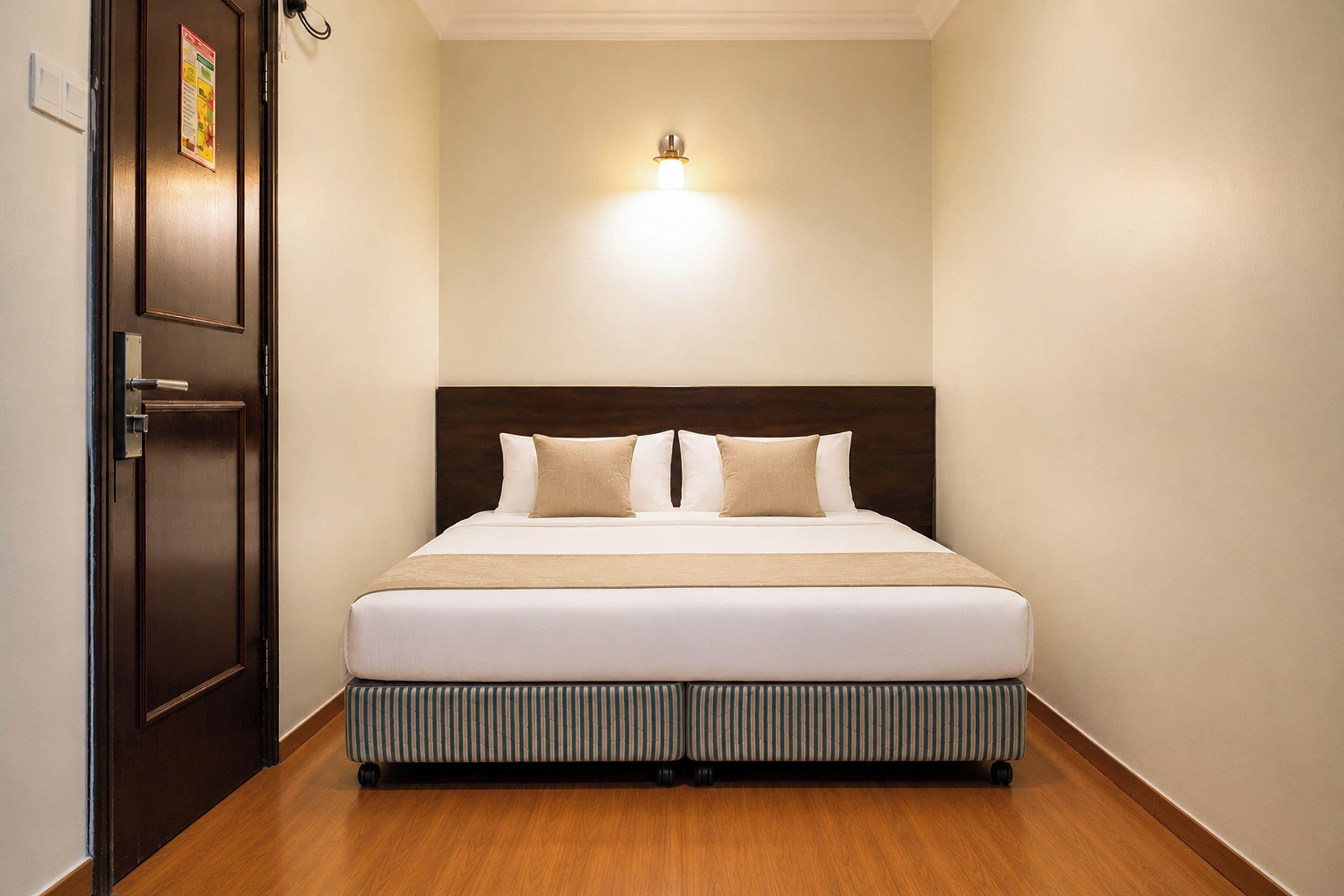 Una camera d'albergo con un letto, una porta e un punto luce a parete.