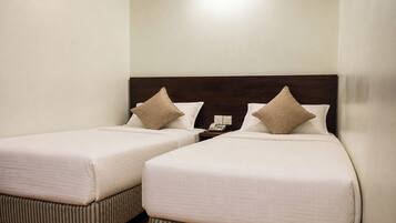 A hotel room with two single beds, each with a pillow and a bedside table with a phone.