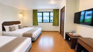 A hotel room with two beds, a television, a desk with a coffee maker, and a window with curtains.