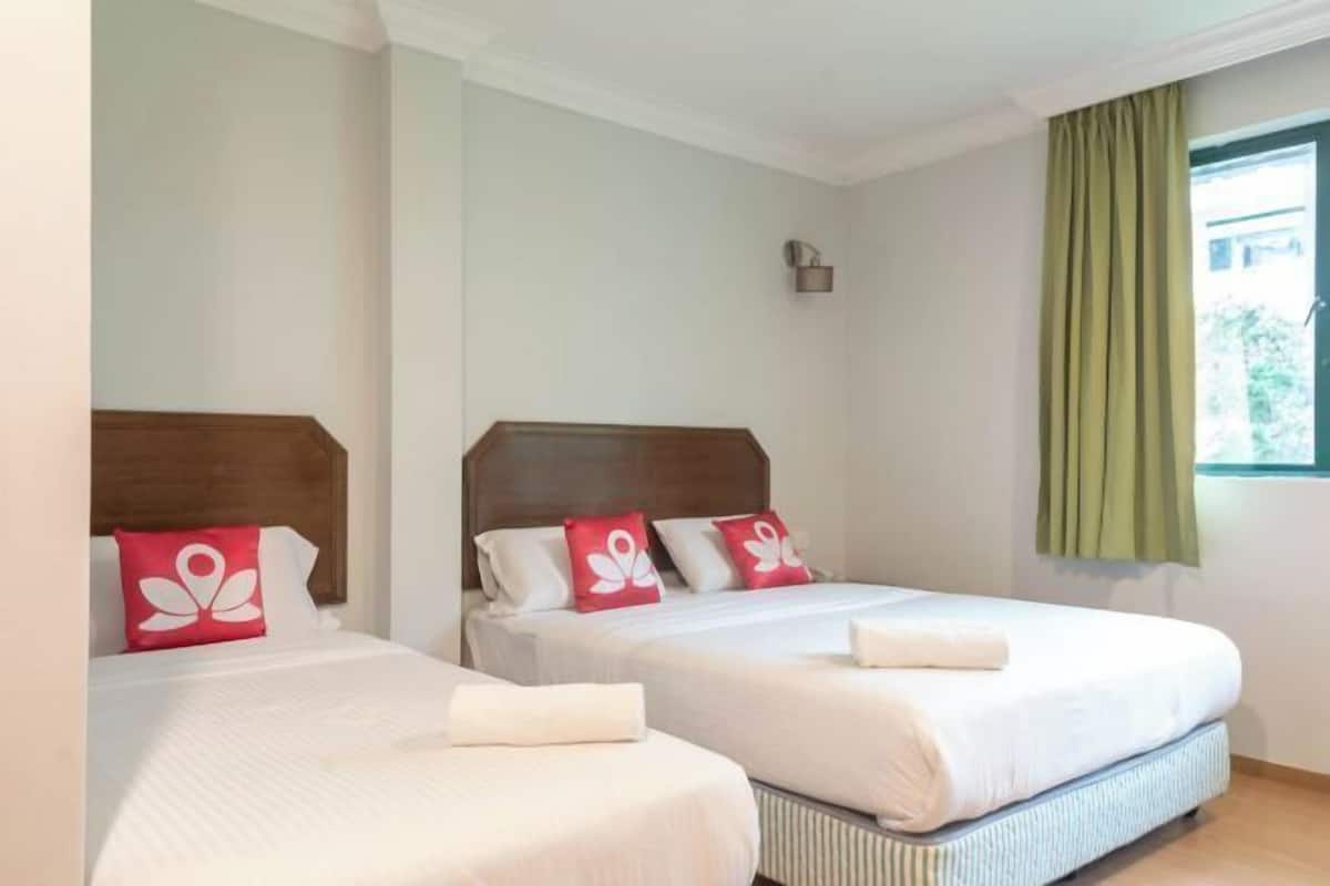 A hotel room with two beds, each with a wooden headboard, white bedding, and red decorative pillows.