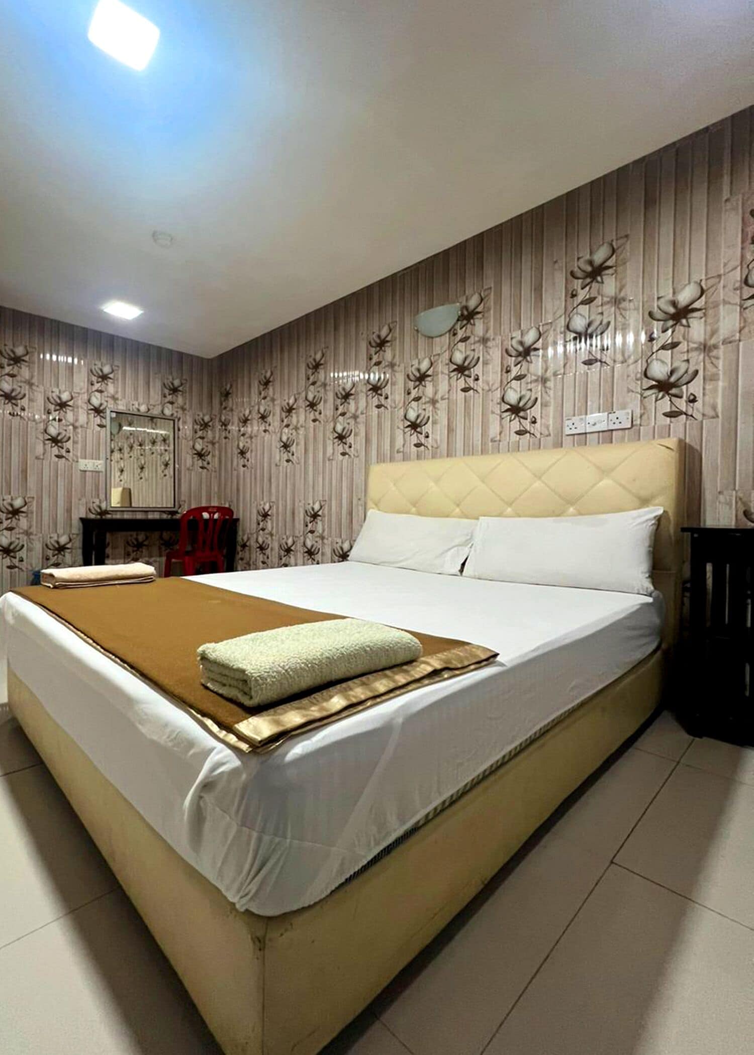Habitación de hotel con una cama grande, una mesita de noche, un espejo y una silla roja.