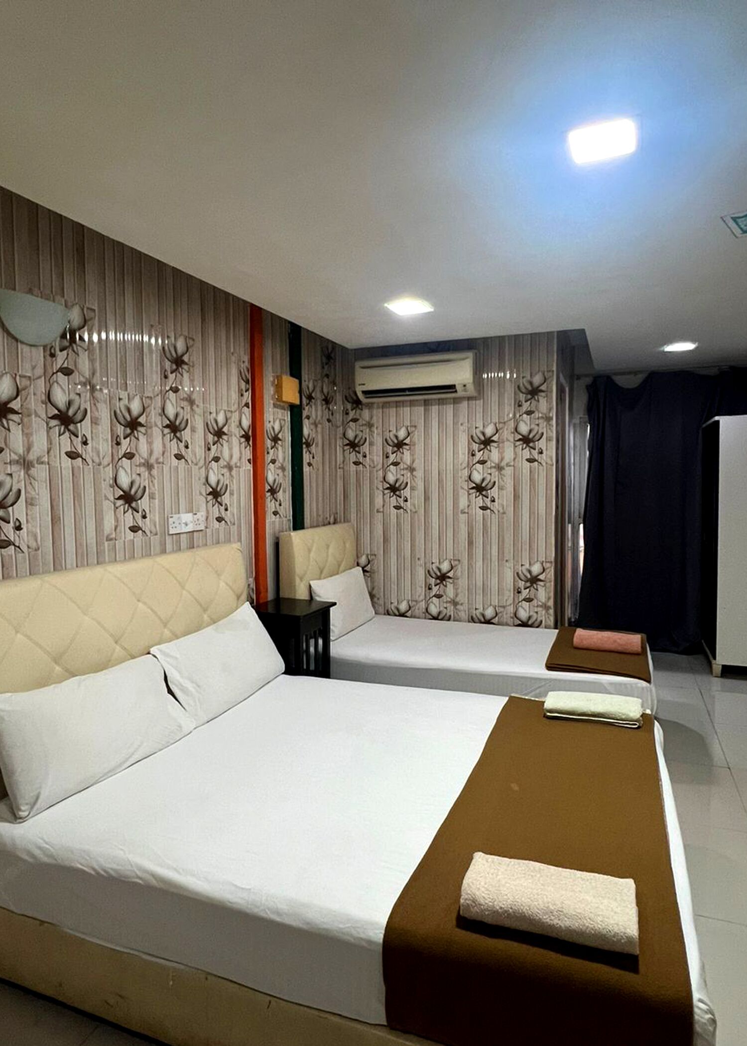 Een hotelkamer met twee bedden, een kleine tafel, een airconditioning en een gordijn.