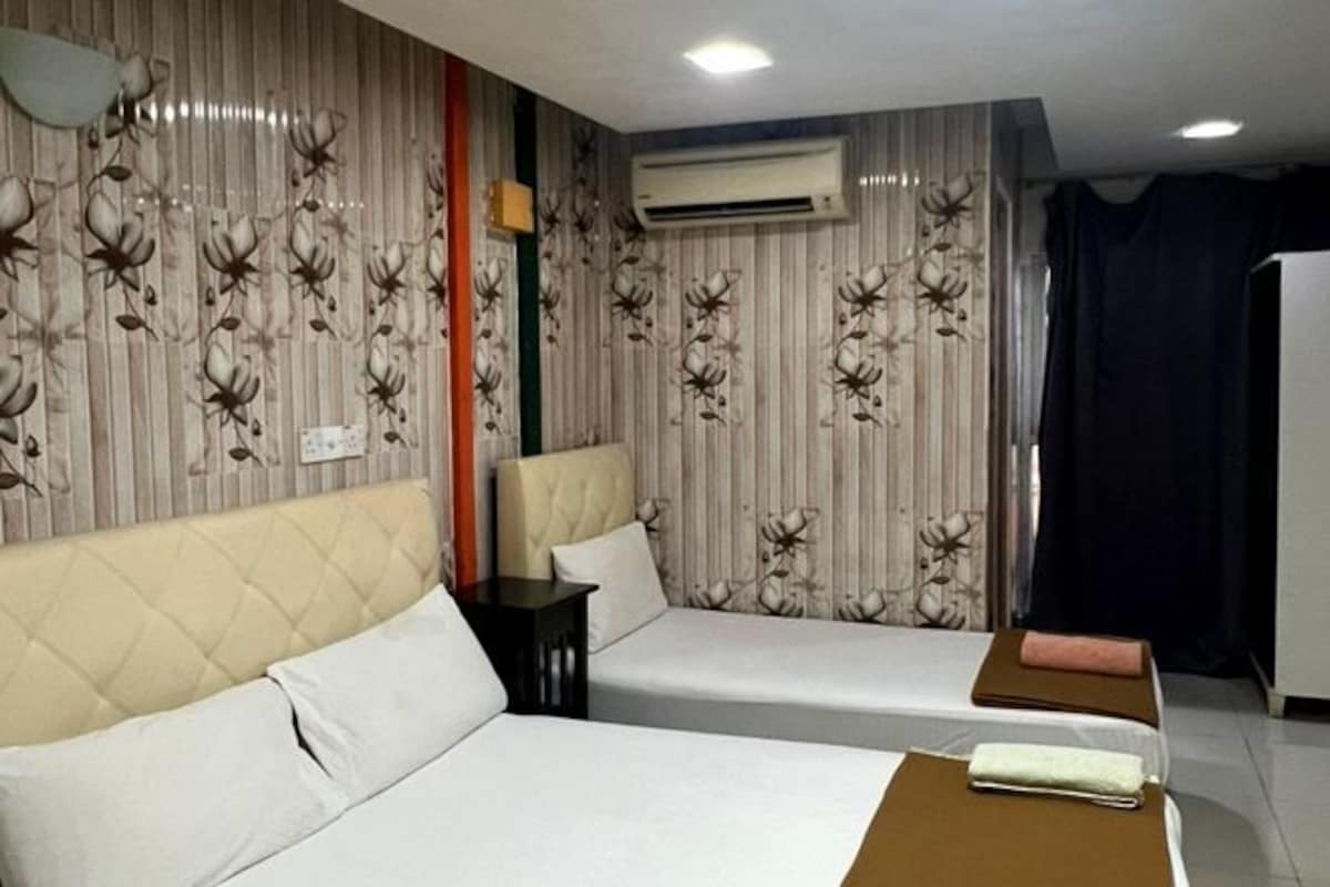 A hotel room with two beds, a small table, and a wall air conditioner.