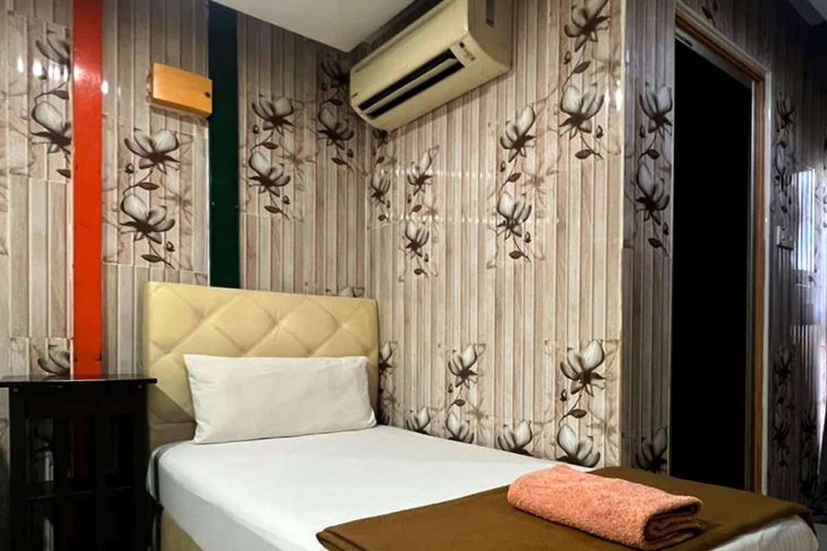 A bedroom with a large bed, an air conditioning unit above it, and a nightstand with a lamp.
