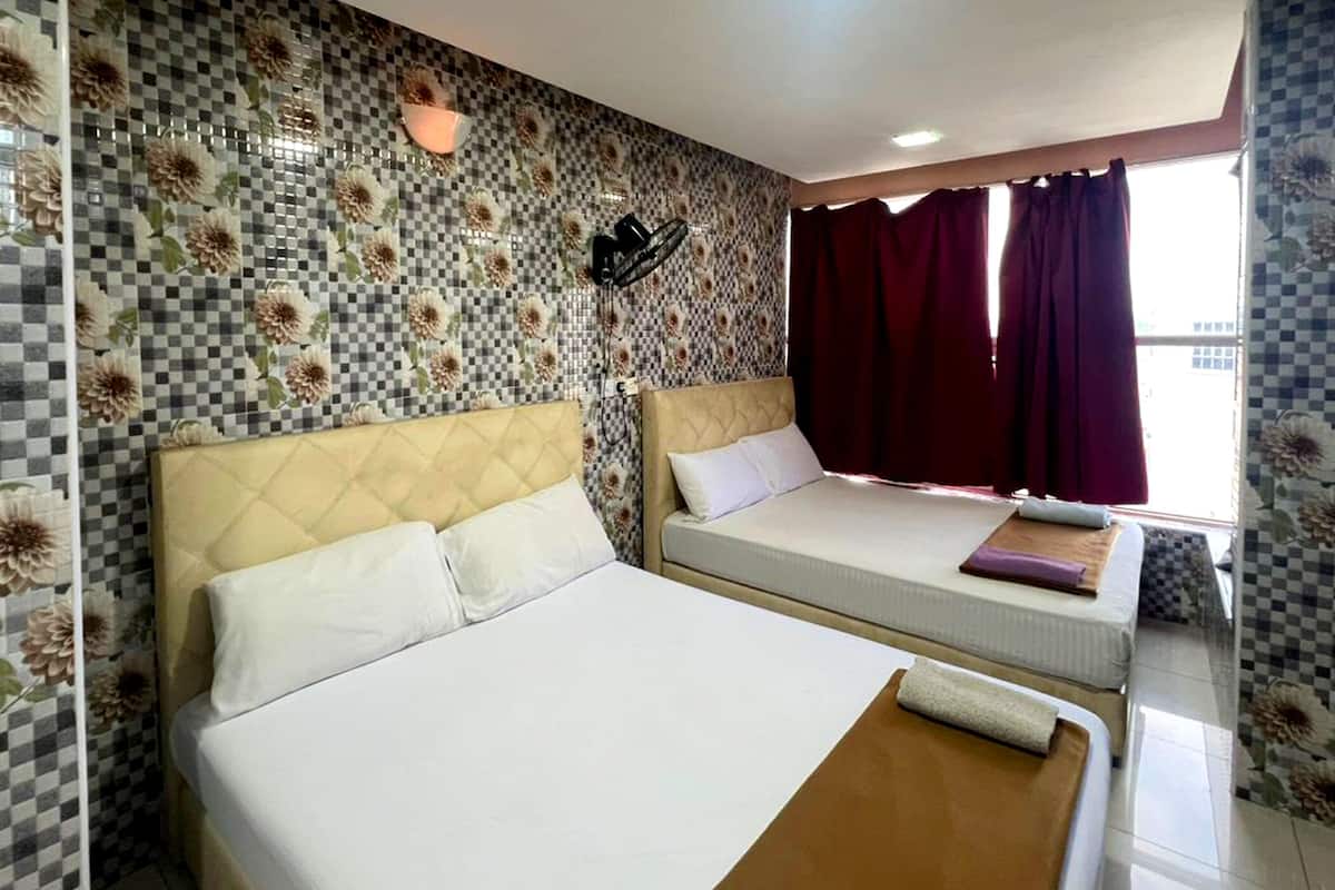 A hotel room with two beds, checkered floral wall tiles, a window with red curtains, and a wall-mounted light fixture.