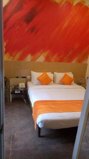 A hotel room with a large bed, two orange pillows, a nightstand, and a wall with a red and orange abstract design. - Sri Balaji Residency (Bengaluru)