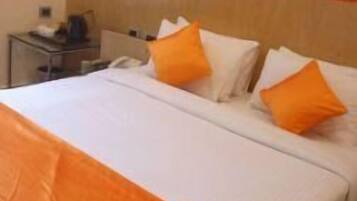 A hotel room with a large bed, white bedding, and orange throw pillows.
