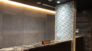 A reception area with a marble counter, a nameplate, a tiled wall, and a modern ceiling with recessed lighting.