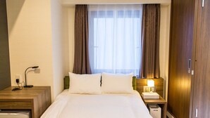 A hotel room with a bed, a nightstand with a lamp, a wooden wardrobe, and a window with curtains.