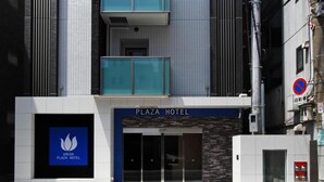 The exterior of Plaza Hotel with a modern facade, a prominent entrance, and a no-parking sign visible.