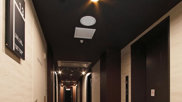 A hotel corridor with a black and beige floor, multiple doors, and ceiling lights.