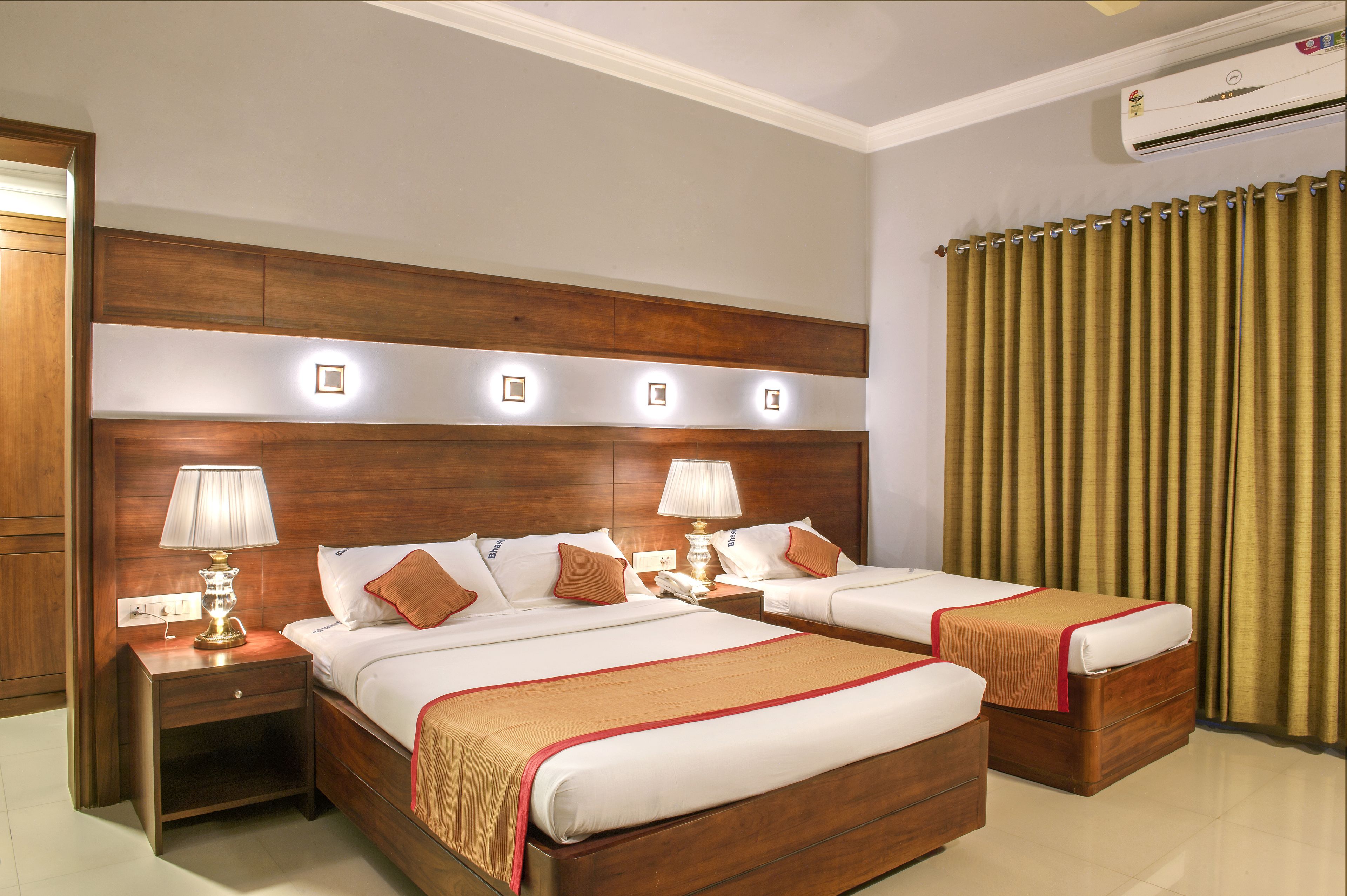 A hotel room with two beds, wooden headboard, bedside lamps, and a large window with curtains.