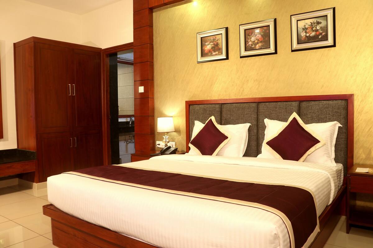 Quarto de hotel com uma cama grande, guarda-roupa de madeira e três quadros florais na parede.