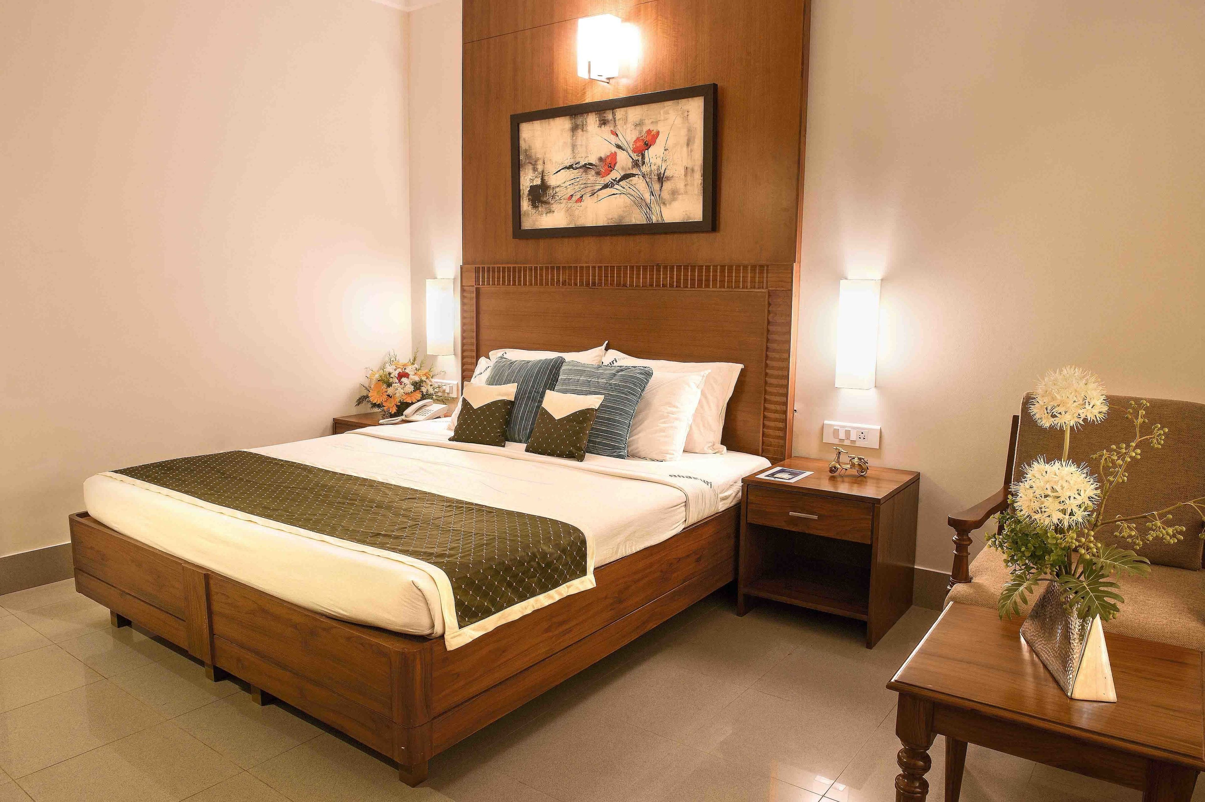A neatly arranged hotel room with a wooden bed, a bedside table with a lamp, a chair, and a wall-mounted artwork.