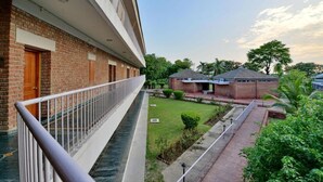 Un edificio con fachada de ladrillo, un balcón con barandilla de metal y un patio ajardinado con un sendero.