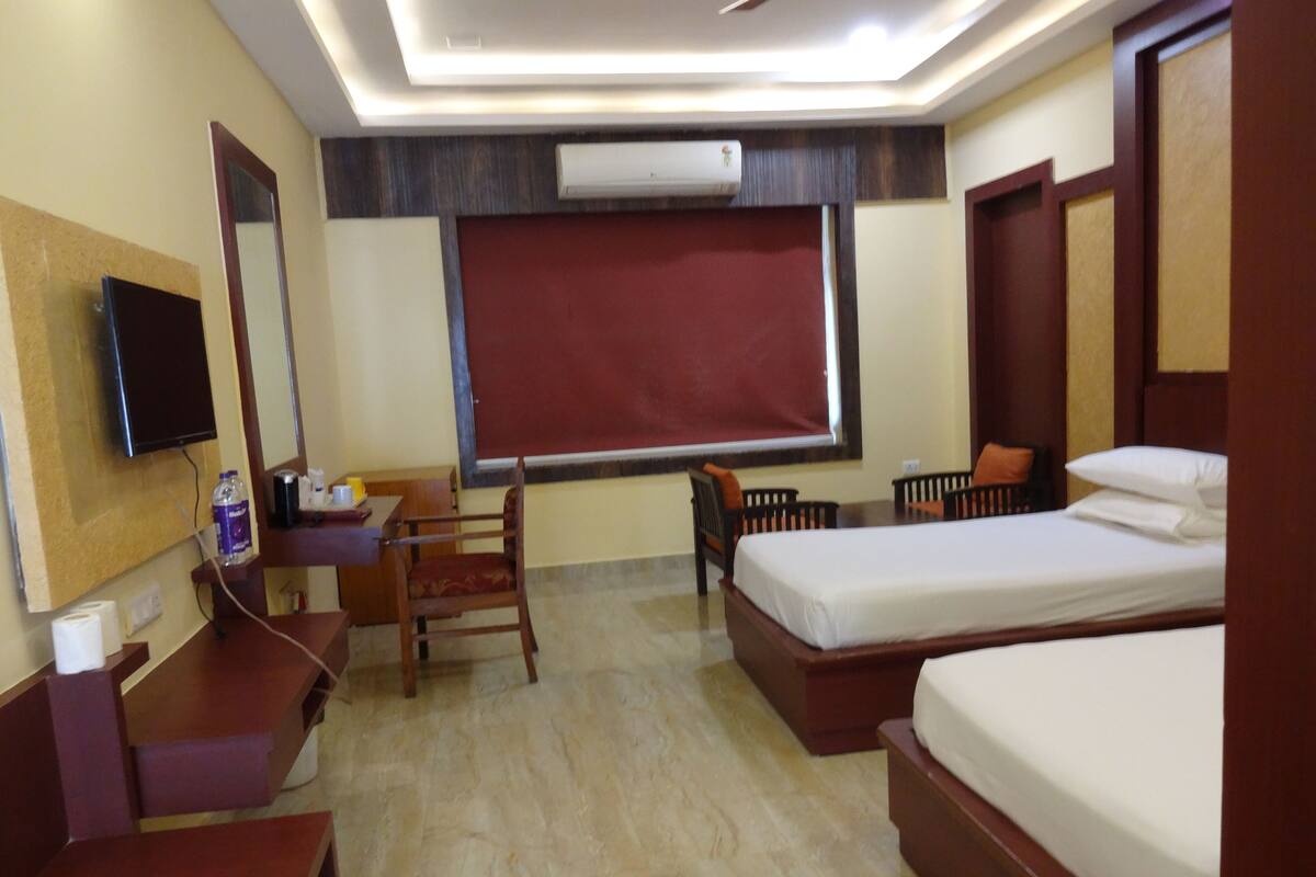 Quarto de hotel com cama, escrivaninha, cadeira e televisão.