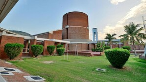 Un edificio con una estructura cilíndrica central, rodeado de un césped cuidado y arbustos podados.