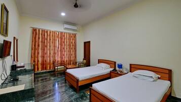 Habitación de hotel con dos camas de madera, suelo de mármol, ventilador de techo, aire acondicionado y televisor sobre un soporte.