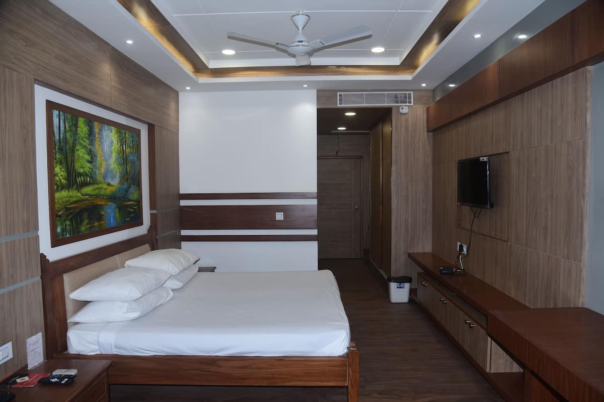 Quarto de hotel moderno com uma cama de madeira, um quadro de uma floresta, um ventilador de teto e uma televisão na parede.