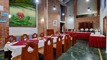 A long dining table with red tablecloths and wooden chairs in a room with brick walls and a mural of a lotus flower.