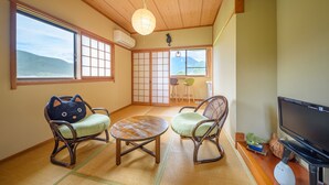 A traditional Japanese room with tatami flooring, a low table, two cat-shaped chairs, a television, and a view of the outdoors. - Yufuin Waraneko no Yado (Yufu)