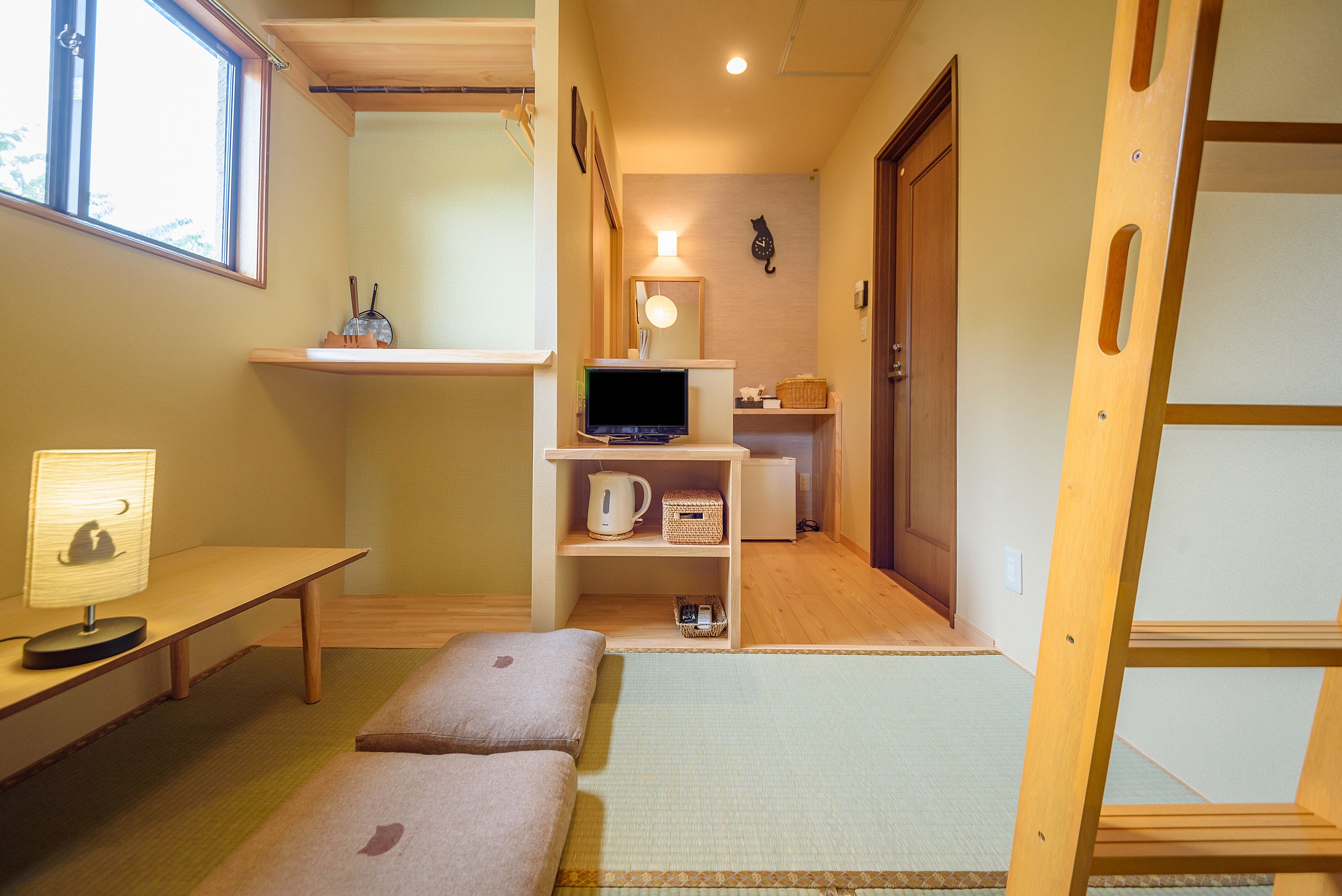 A compact room with a desk, a shelf with a kettle, a television, and a ladder.