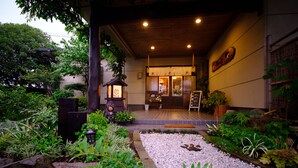 A traditional Japanese building with a wooden entrance, a stone pathway, and a garden with various plants and a lantern. - Yufuin Waraneko no Yado (Yufu)