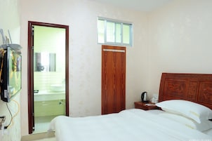 Un dormitorio con cabecera de madera, una cama individual, una mesita de noche con un teléfono y una taza, y una ventana sobre la puerta.