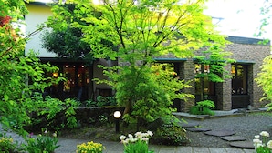 A garden with potted plants and a stone pathway leading to a building with a stone facade and windows. - Yufuin Onsen Ryokan Hananomai (Yufu)