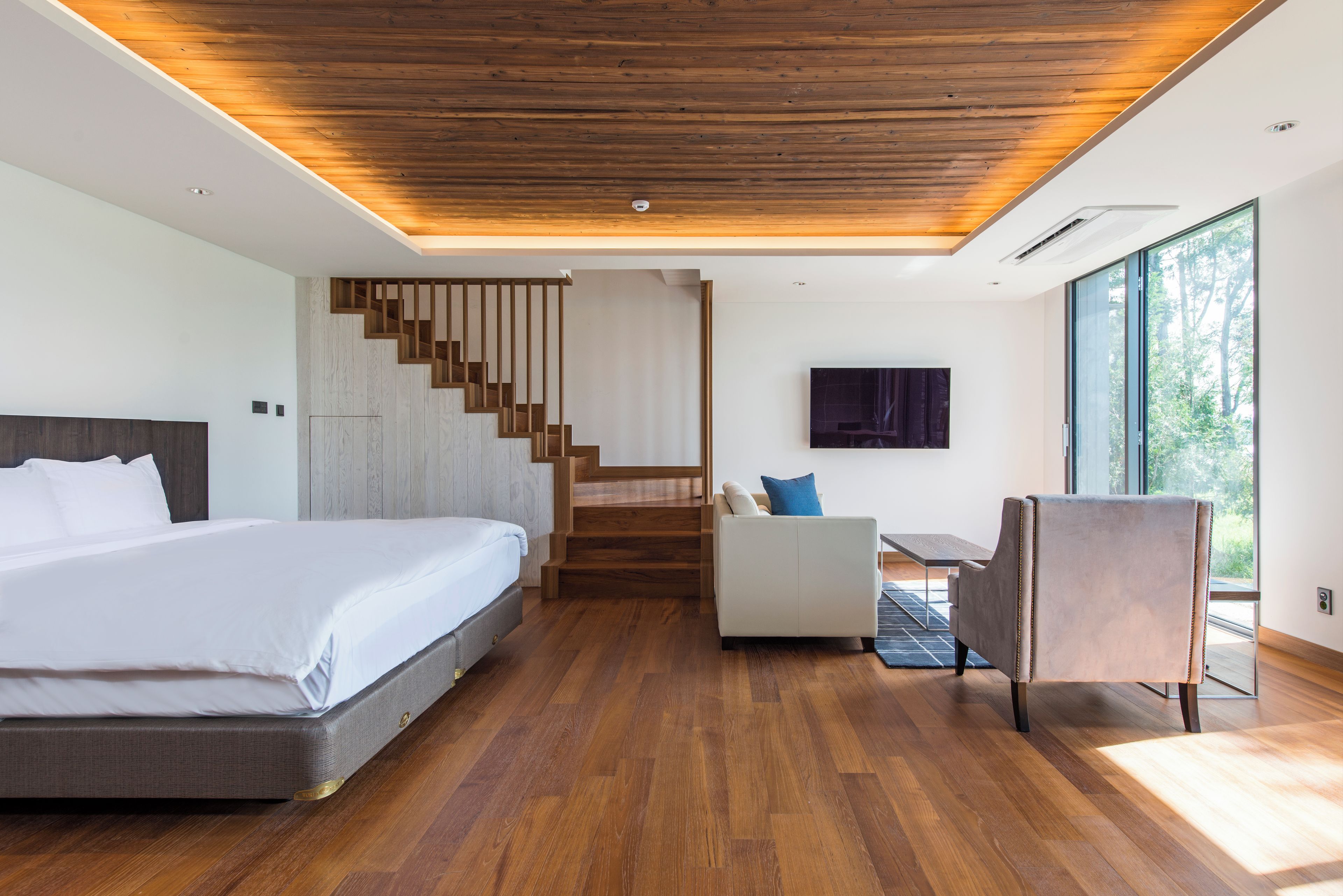 A modern bedroom with a large bed, a desk, a chair, and a staircase.