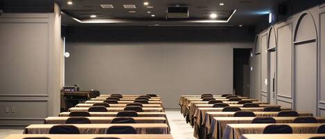 A conference room with rows of tables and chairs, a podium, and a large grey wall.