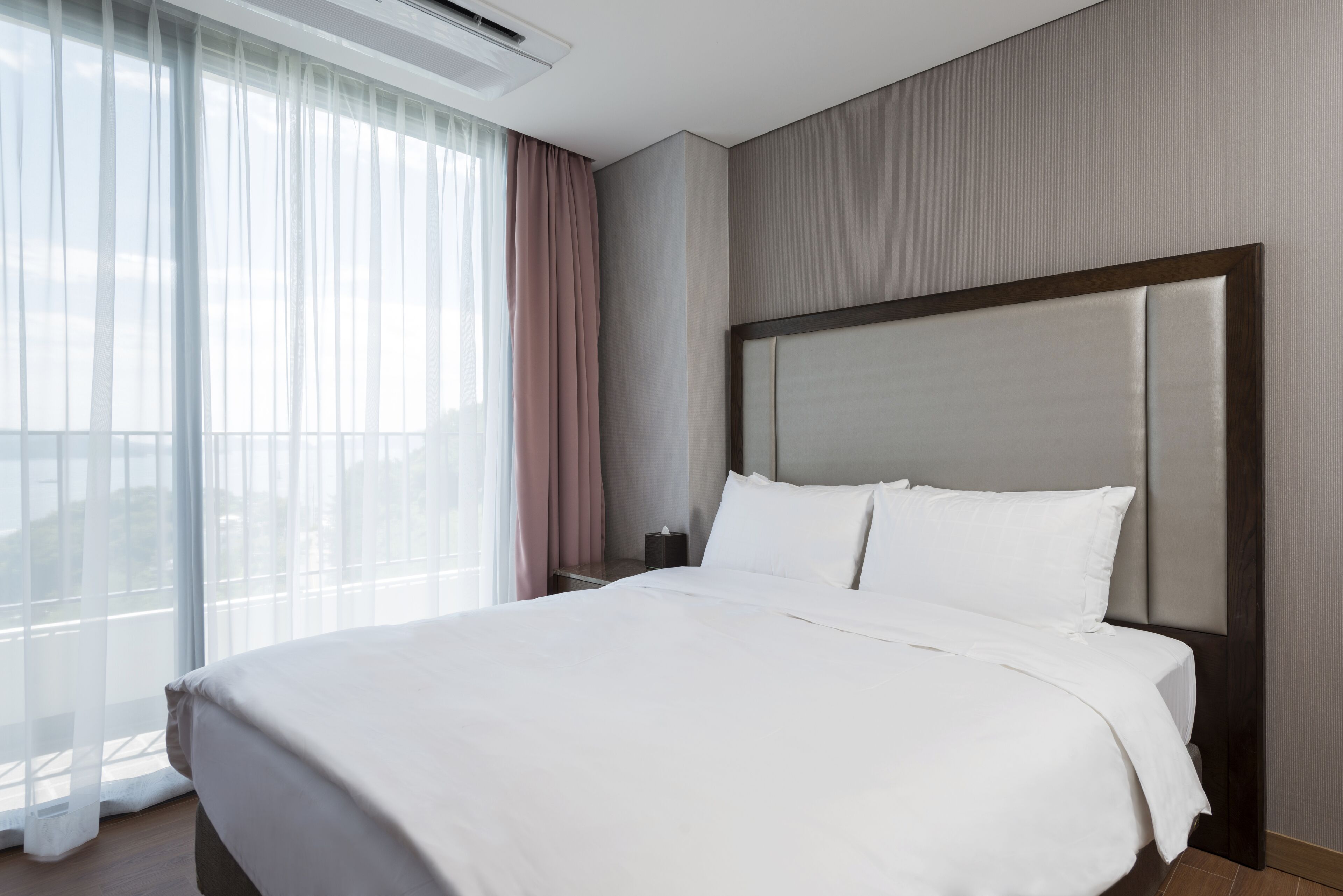 Une chambre d’hôtel avec un grand lit, une table de chevet, une fenêtre avec des rideaux légers et une vue sur l’extérieur.