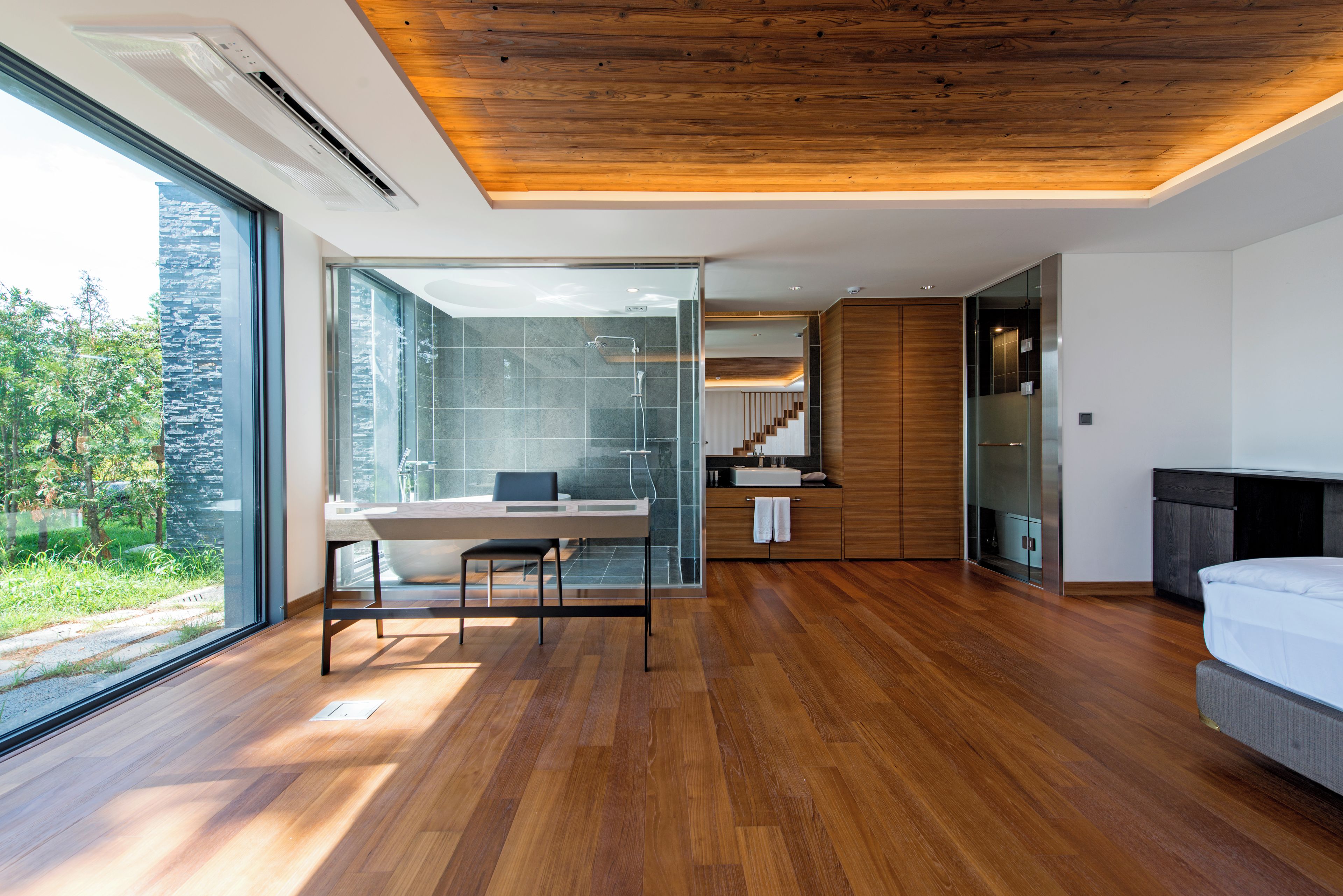 Un dormitorio moderno con techo de madera, un ventanal grande y vistas al verdor.