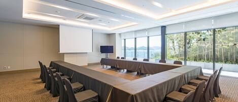 Una sala de conferencias con una larga mesa, sillas y una pantalla para proyector.