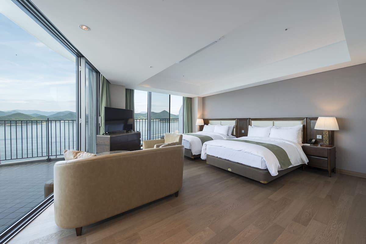 Una habitació d'hotel moderna amb un balcó, dues lliteres, un sofà i una televisió.