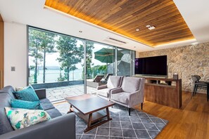 Una sala de estar moderna con sofá, mesa de centro y televisor. Se aprecia una pared de piedra y un techo de madera.