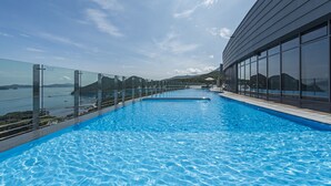 A swimming pool with clear blue water, surrounded by glass railings and a modern building with large windows. - Stanford Hotel & Resort Tongyeong (Tongyeong)