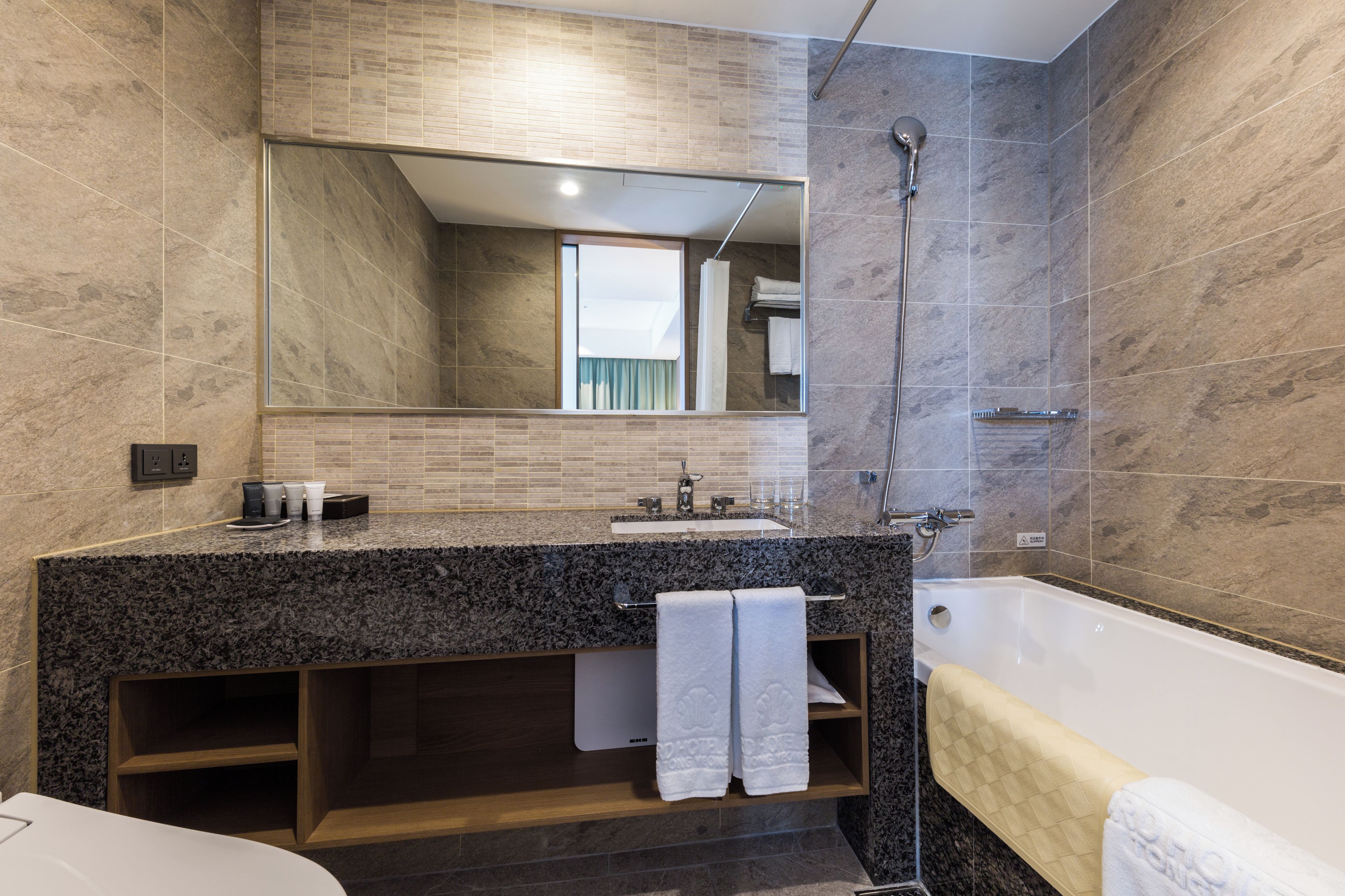 Ein modernes Badezimmer mit einer Granit-Arbeitsplatte, einem großen Spiegel, einer Badewanne und einer Dusche.