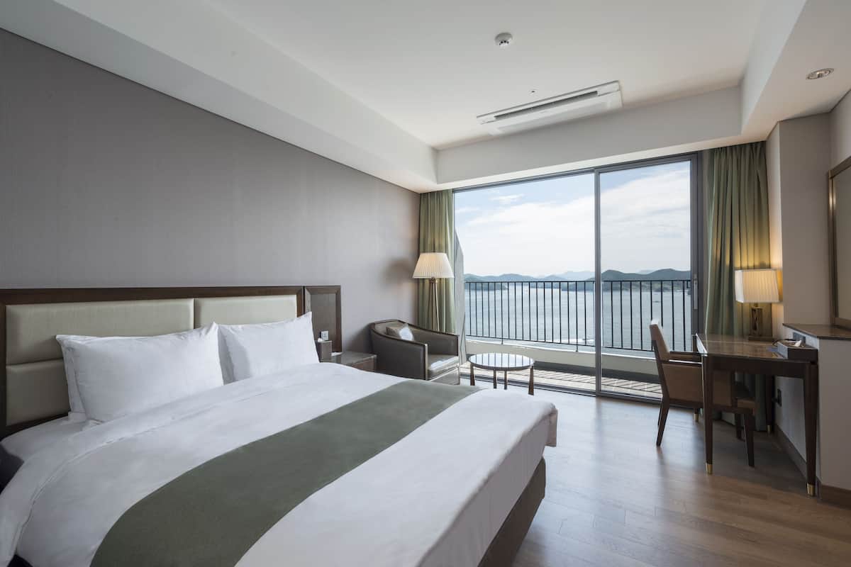 Habitació d'hotel amb un llit gran, una taula de treball, una cadira i vista al mar.