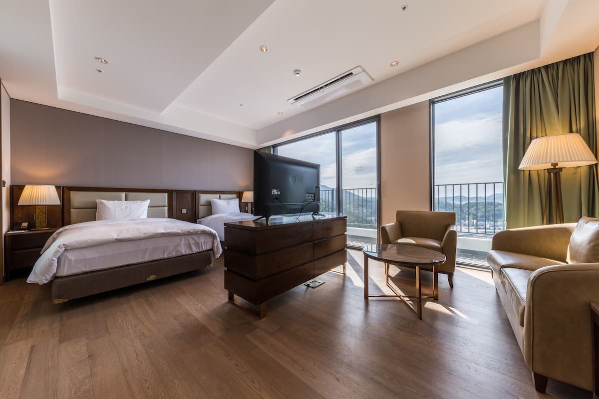 Habitació d'hotel moderna amb un llit gran, una petarrera, una televisió, un sofà i un balcó amb vistes.