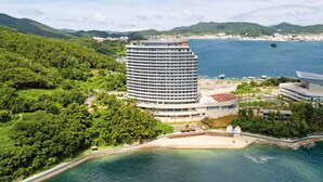A high-rise hotel with a circular design, located near a beach and surrounded by lush greenery and mountains. - Stanford Hotel & Resort Tongyeong (Tongyeong)