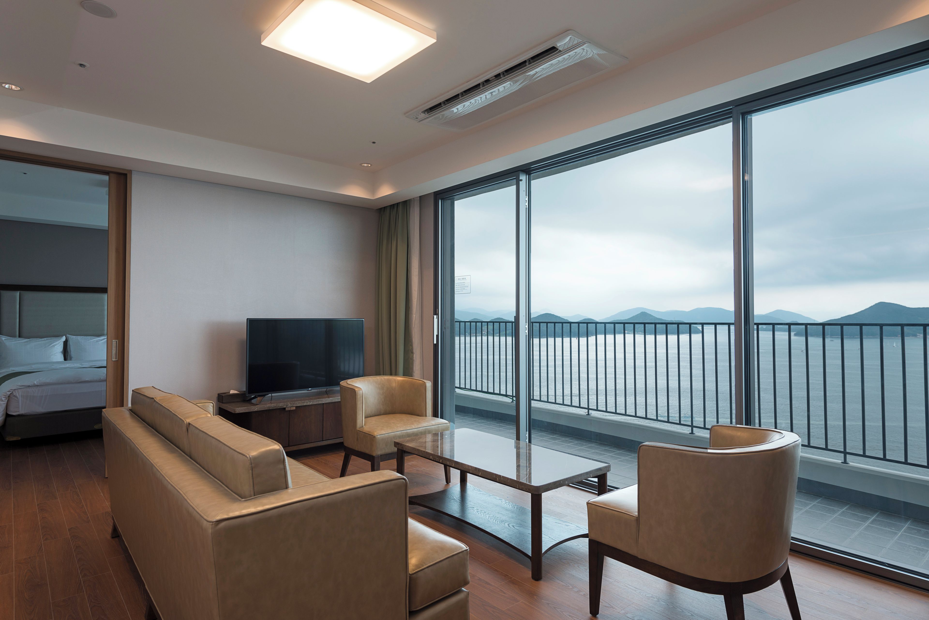 A modern hotel room with a large window, a bed, a TV, and a seating area.