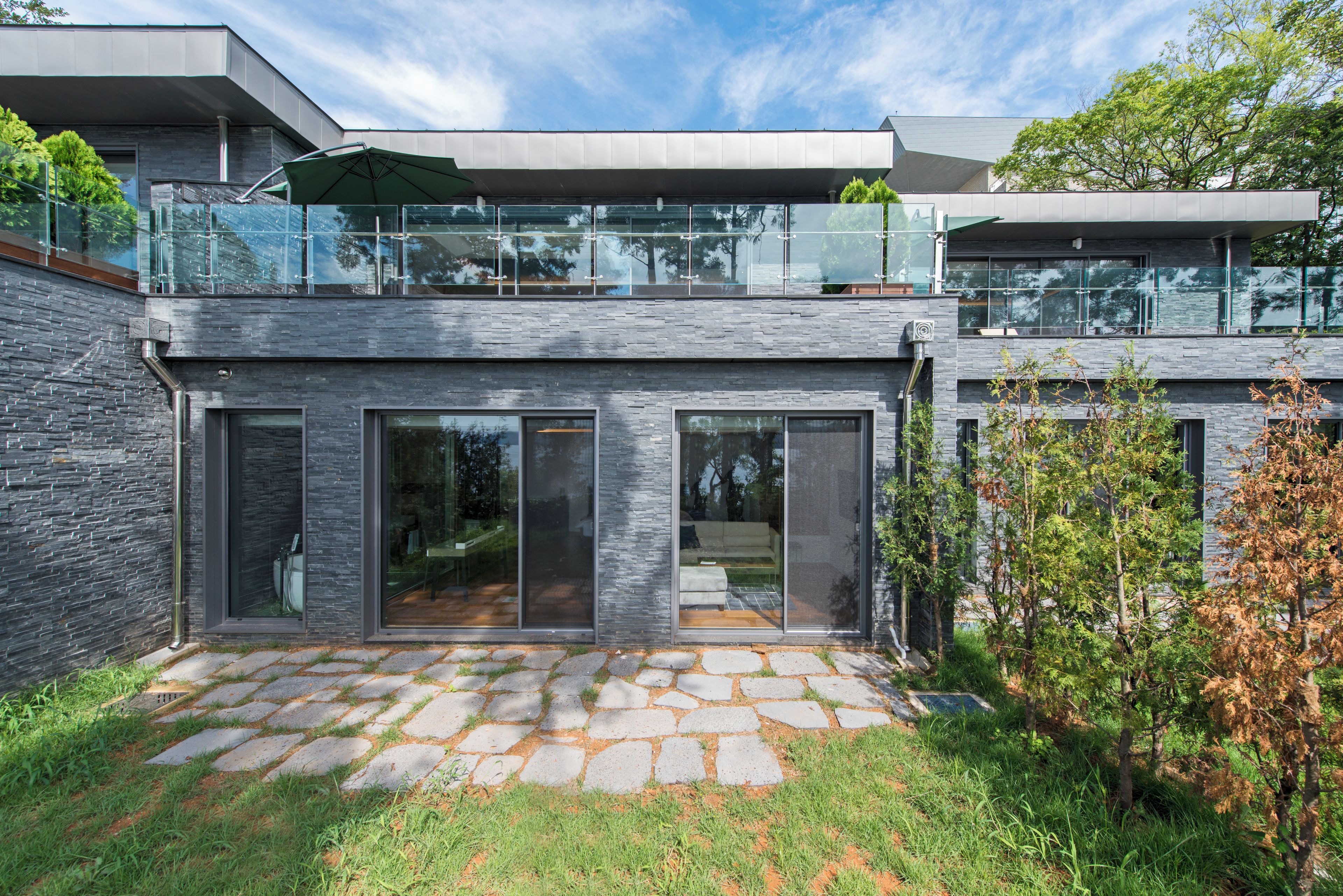 A modern house with a stone facade, large glass windows, and a stone pathway leading to the entrance.